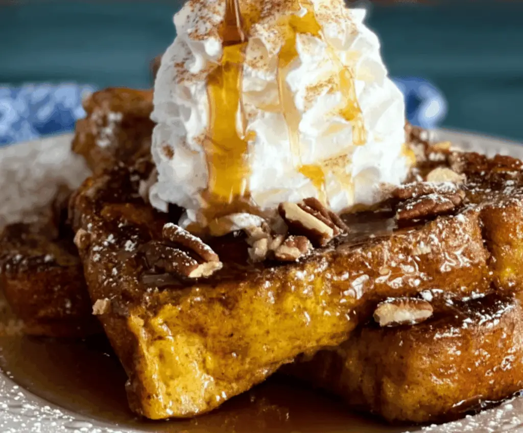 Delicious Pumpkin Pie French Toast topped with whipped cream and cinnamon, served with fresh orange slices on a plate.