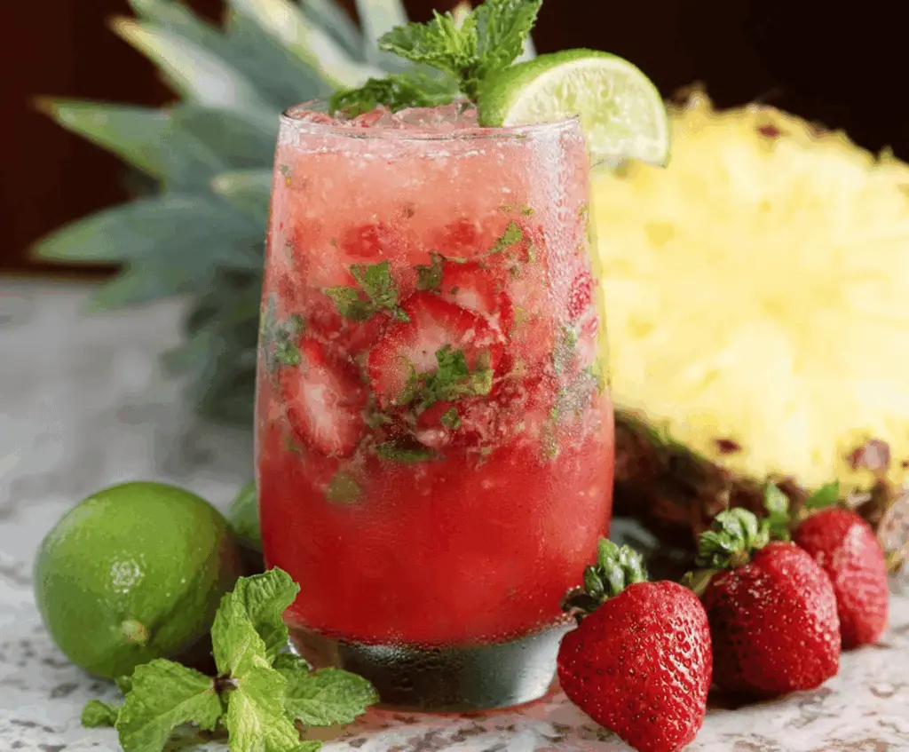 Fresh strawberry and pineapple mojito cocktail with mint leaves, lime wedges, and crushed ice in a glass, perfect for summer drinks.